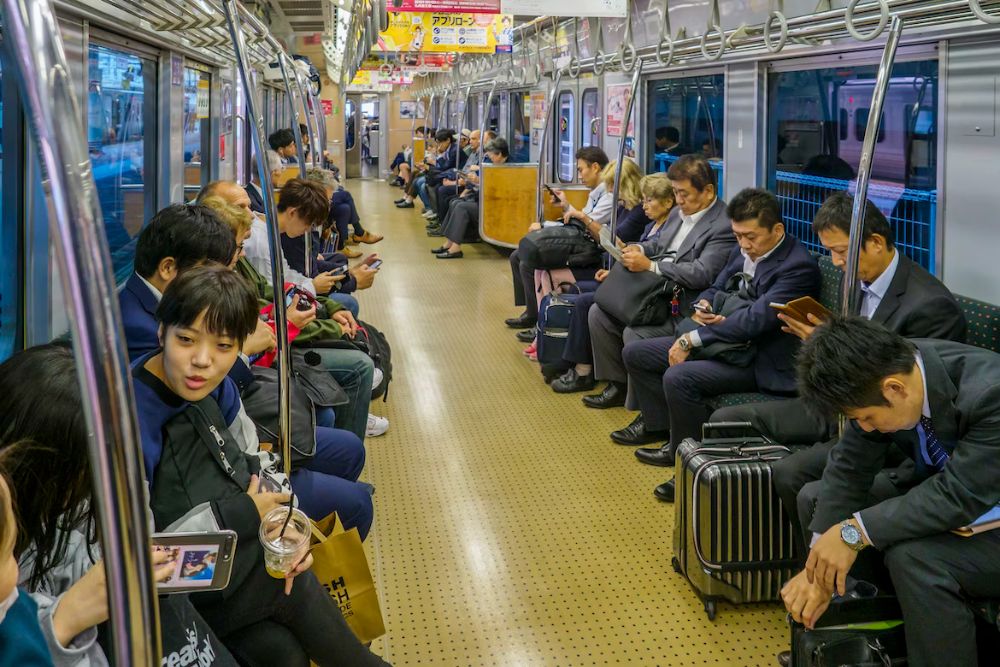 A busy Japanese train carriage with people talking to each other and other people using their phones or reading books