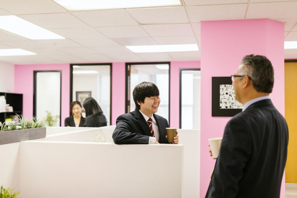 Two Japanese male office workers wearing business suits are smiling and laughing, enjoying a conversation over a cup of coffee