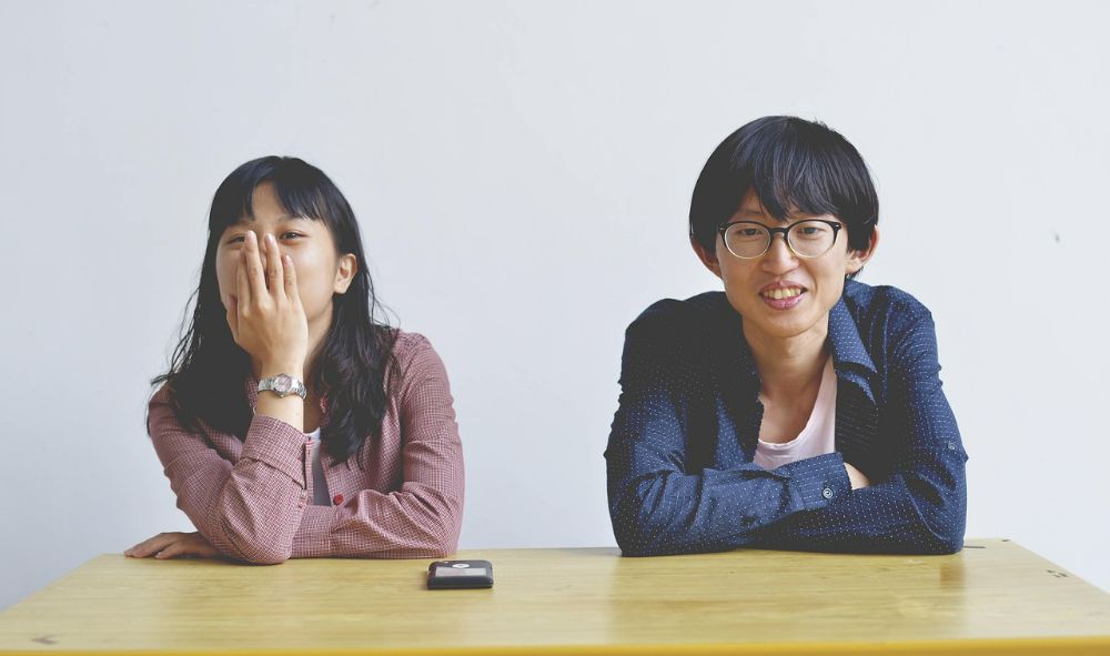 Two Japanese friends sat at a table together looking happy, one female and one male