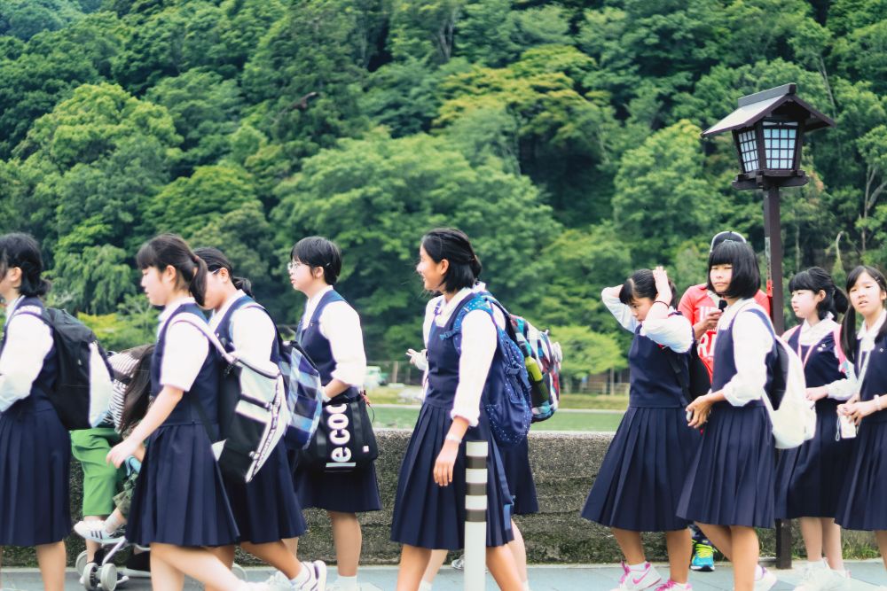 A group of Japanese schoolgirls walking through a park together in their uniform