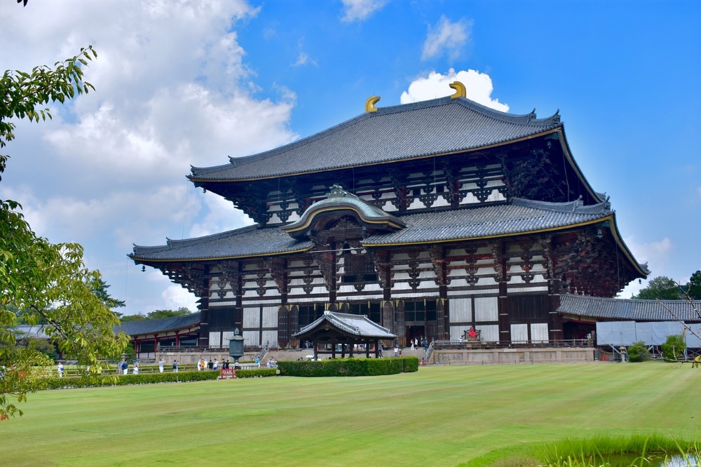 A large brown and white traditional Japanese building with a blue cloudy sky in the background and a neatly kept lawn in the foreground